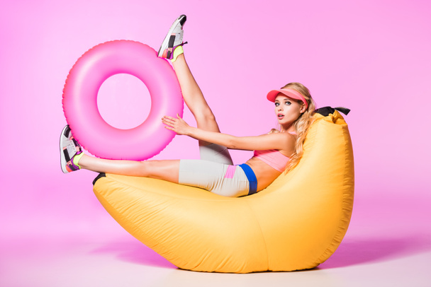 aantrekkelijk meisje op Bean Bag Chair met opblaasbare zwemmen ring op roze, pop concept - Foto, afbeelding