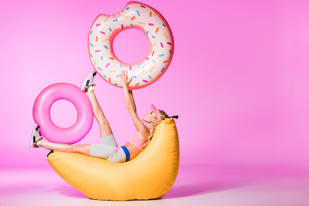 attractive girl on bean bag chair with inflatable swim rings on pink, doll concept - Фото, зображення