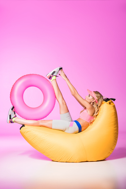 aantrekkelijk meisje op Bean Bag Chair met zwemmen ring op roze, pop concept - Foto, afbeelding