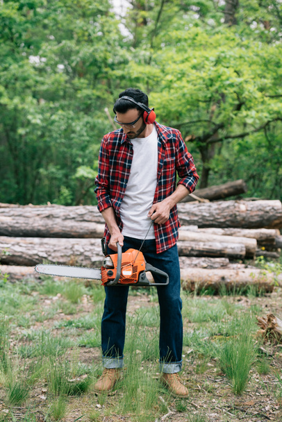 lumberjack in checkered shirt and noise-canceling headphones adjusting chainsaw  - Photo, Image