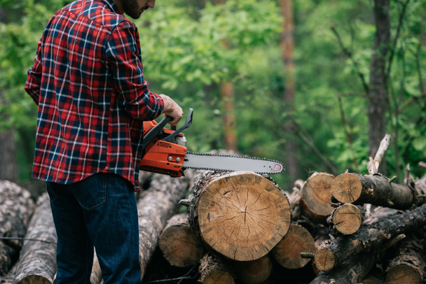 partial view of lumberjack cutting trunk with chainsaw in forest - Foto, Imagem