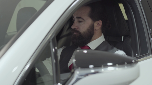 Successful man sitting in passenger compartment of the new vehicle inspects the interior of the newly purchased auto from the dealership. Car showroom. Advertising concept. - Video