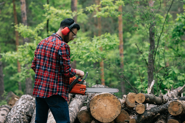 bûcheron barbu en chemise à carreaux troncs de coupe avec tronçonneuse en bois
 - Photo, image