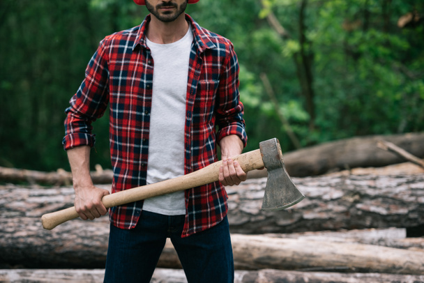 cropped view of lumberman in plaid shirt holding axe in forest - Zdjęcie, obraz
