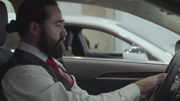 Portrait attractive successful bearded businessman sitting in the vehicle and inspects newly purchased auto from the car dealership. Car showroom. Advertising concept. - Video