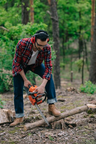 lumberjack in noise-canceling headphones cutting wood with chainsaw in forest - Photo, Image