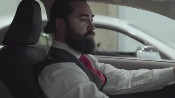 Portrait attractive successful bearded businessman sitting in the vehicle and inspects newly purchased auto from the car dealership. Car showroom. Advertising concept. - Filmagem, Vídeo