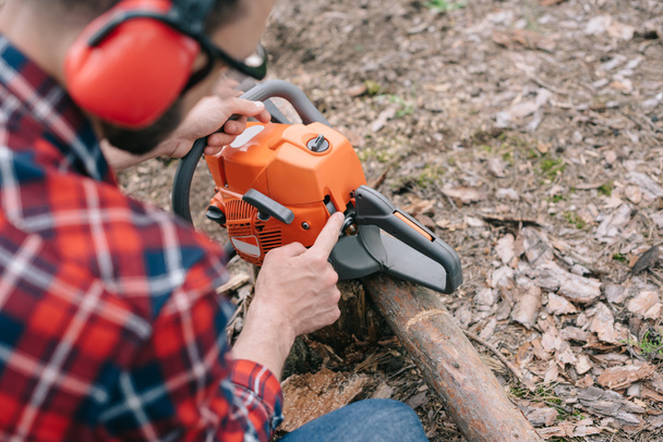selective focus of lumberjack in hearing protectors repairing chainsaw in forest - Photo, Image