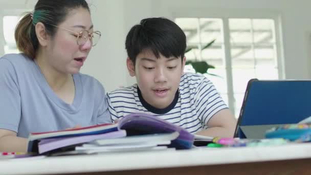 Mutter hilft ihrem Sohn bei den Hausaufgaben zu Hause. schöne Mutter, die Schulbücher liest und mit ihrem Sohn spricht, während sie zu Hause gemeinsam Hausaufgaben macht. - Filmmaterial, Video