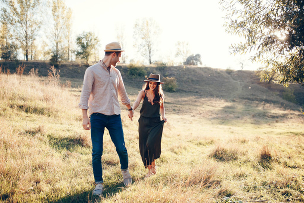 Kültéri felvétel fiatal párról, akik kéz a kézben sétálnak át a réten. Férfiak és nők beszélgetnek, sétálnak a fűmezőn vidéken..  - Fotó, kép