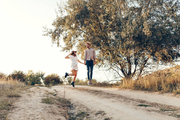 Stilvolles Paar, das mit einem Glas Wein auf dem Rasen im Freien spaziert. Mann und Frau schauen einander an und gehen gemeinsam ins Freie. - Foto, Bild