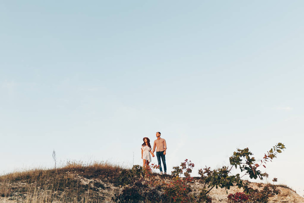 芝生のフィールドで彼氏と一緒に歩いている若い女性の背面ショット。牧草地を散策を楽しんでいるカップル. - 写真・画像