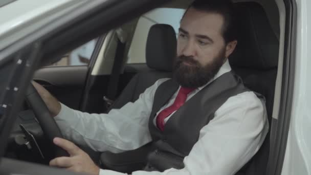 Portrait attractive confident bearded businessman sitting in the vehicle and inspects newly purchased auto from the car dealership. Car showroom. Advertising concept. - Video