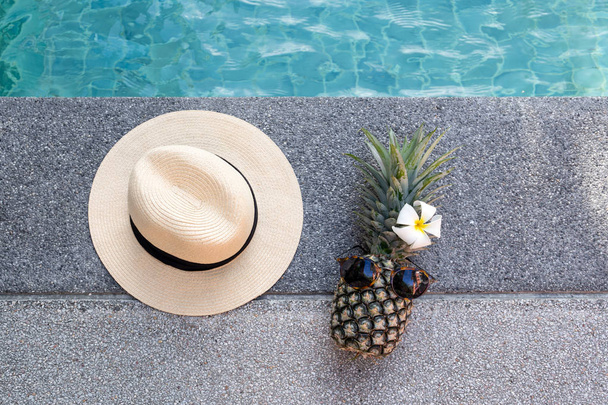 Yüzme Havuzu tarafından güneş gözlüğü ve çiçek ve şapka ile komik ananas. - Fotoğraf, Görsel