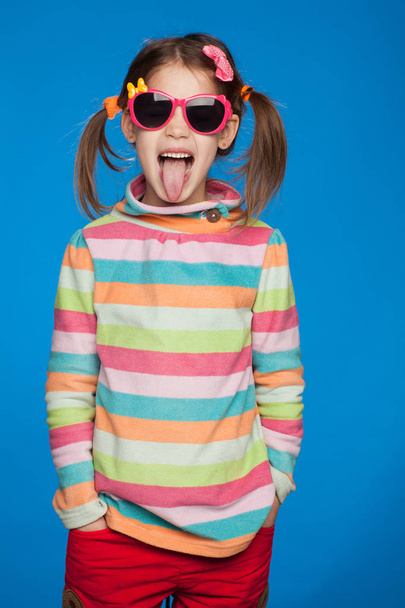 Portrait of an emotional girl of five years old in a striped sweater and in children's glasses on a blue background - Foto, afbeelding