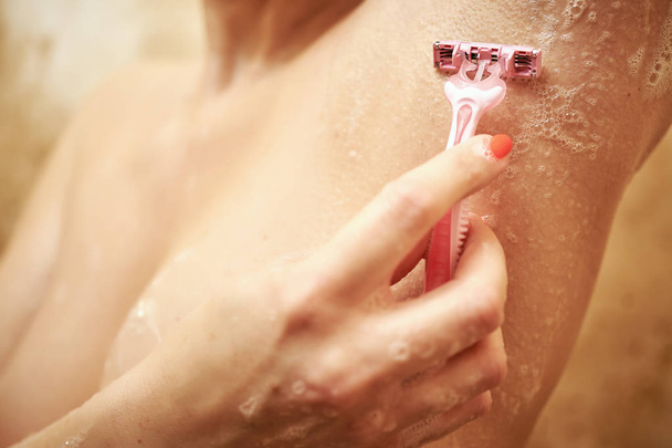 verschwommener Blick auf sexy Mädchen in der Dusche hinter nassem Glas, das sich rasiert . - Foto, Bild