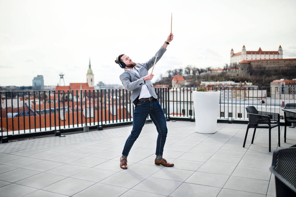 A young businessman with headphones standing on a terrace, having fun. - Фото, изображение