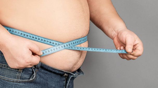 Un hombre mide su vientre gordo con una cinta métrica. en una ba gris
 - Foto, Imagen