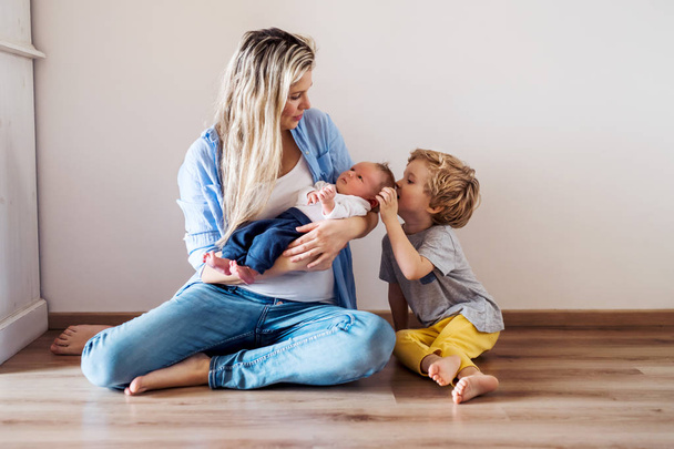 A beautiful young mother with a newborn baby and his brother at home. - Foto, Bild