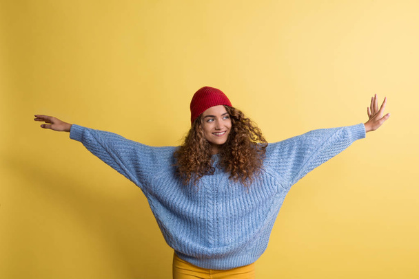 Portrait of a young woman with woolen hat in a studio on a yellow background. - Fotografie, Obrázek
