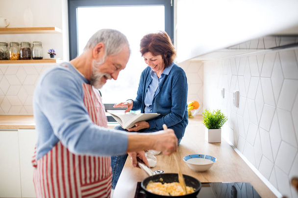 A portrait of senior couple in love indoors at home, cooking. - Fotó, kép