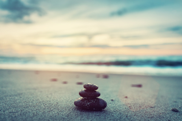Close view of stone pyramid made of pebbles on sandy beach at sunset - Photo, Image