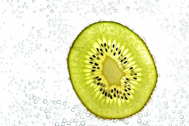 A sliced kiwi lies on a light background - through the thin kiwi slices are illuminated from below  - Фото, зображення