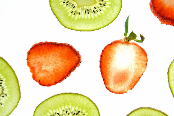 Un kiwi en rodajas y una fresa en rodajas se encuentran sobre un fondo blanco brillante iluminado desde arriba - concepto con frutas frescas
  - Foto, imagen