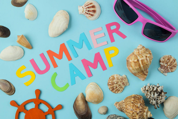 Text SUMMER CAMP of multicolored paper letters and sunglasses and seashells on a bright blue background. top view. flat lay - Photo, Image