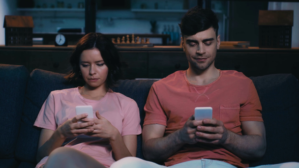 junge Männer und Frauen sitzen auf der Couch und benutzen Smartphones, während neugierige Mädchen auf den Smartphone-Bildschirm ihres Freundes schauen - Filmmaterial, Video