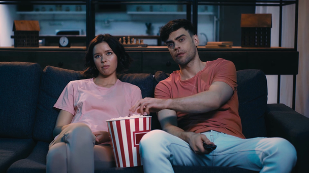 vervelen jonge man en vrouw zittend op de Bank, het eten van popcorn en het gebruik van afstandsbediening terwijl TV kijken - Video