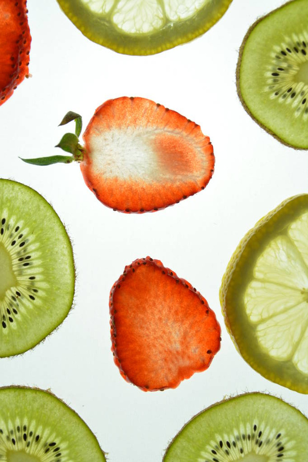 A különböző szeletelt gyümölcsök, mint a narancs, eper és Kiwi fekszik egy fényes, fehér háttér, és megvilágított felülről fény-koncepció, friss és egészséges gyümölcsök különböző színekben -  - Fotó, kép