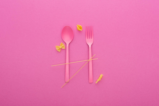 růžová plastová lžíce a vidlička a čtyři různé druhy těstovin izolovaných na růžovém - Fotografie, Obrázek