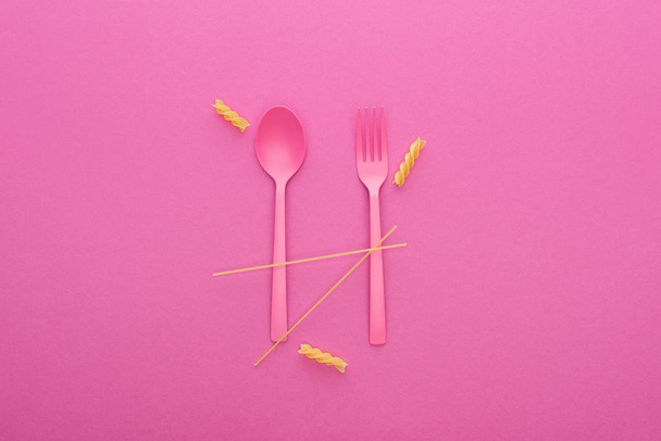 pink plastic spoon and fork and two different kinds of pasta isolated on pink - Фото, изображение