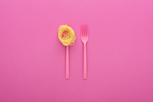 pink plastic fork and pasta on pink spoon on pink background - Фото, изображение