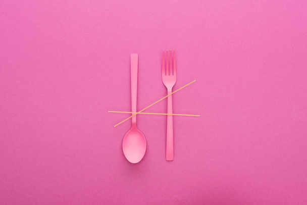 pink plastic spoon upside down and fork with spaghetti isolated on pink - Foto, Imagen
