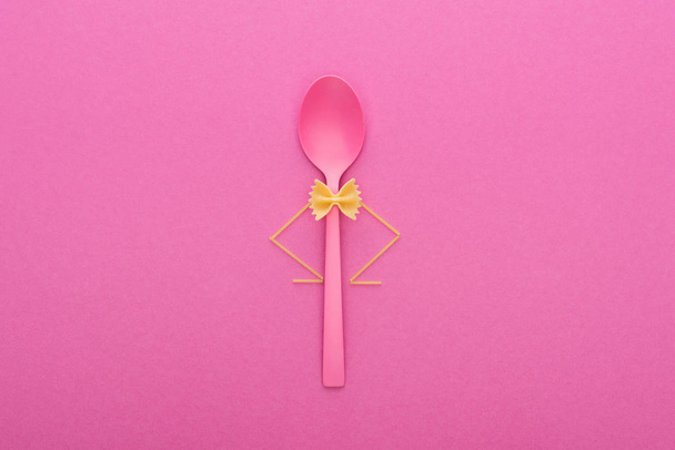 pasta farfalle sin cocer en cuchara de plástico y espaguetis aislados en rosa
 - Foto, Imagen
