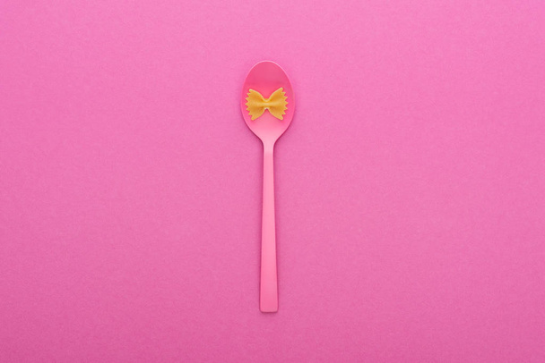 pasta farfalle sin cocer en un tazón de cuchara de plástico aislado en rosa
 - Foto, imagen
