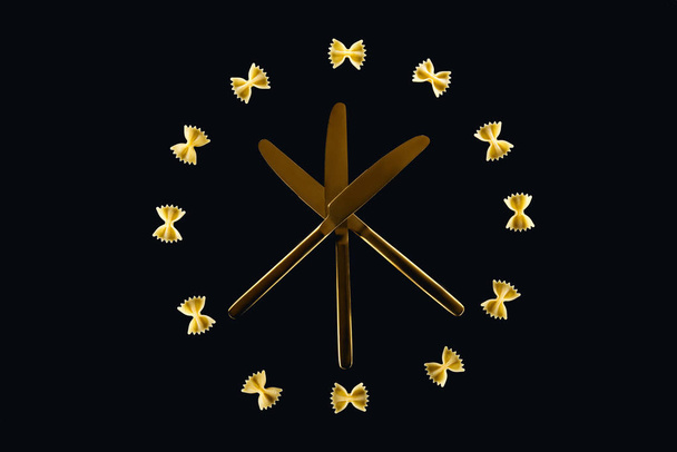 vista superior de pasta farfalle en círculo con tres cuchillos cruzados en medio aislados en negro
 - Foto, Imagen