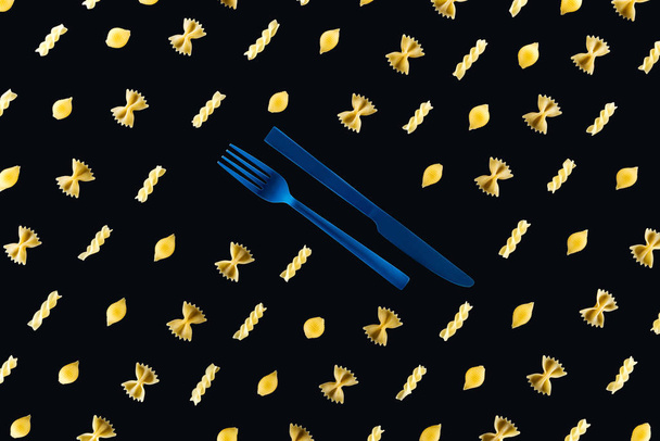 flache Lage verschiedener Nudelsorten mit blauer Gabel und Messer aus Kunststoff in der Mitte isoliert auf schwarz - Foto, Bild