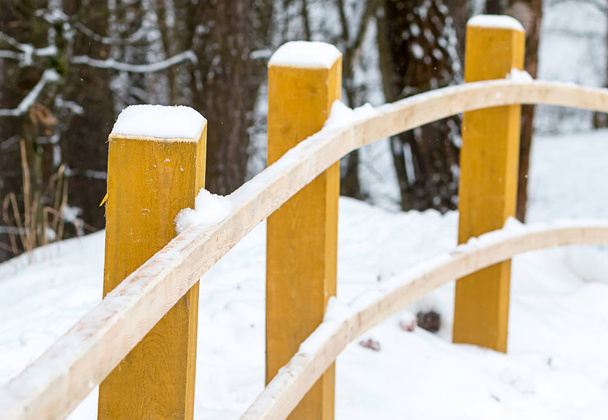 Деревянный столб перила изогнуты бежевый забор зимней дороге в лесу. Желтая снежная шапочка - Фото, изображение