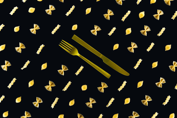 disposición plana de diferentes tipos de pasta con tenedor amarillo plástico y cuchillo en medio aislado en negro
 - Foto, imagen