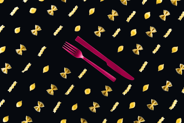 επίπεδη μορφή των διαφορετικών ειδών ζυμαρικών με πλαστικό ροζ πιρούνι και μαχαίρι στη μέση απομονωμένη σε μαύρο - Φωτογραφία, εικόνα