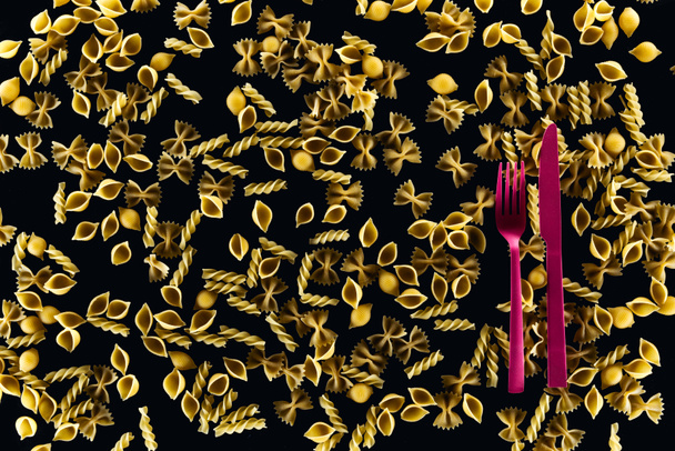 ylhäältä näkymä muovista vaaleanpunainen haarukka ja veitsi sekoitettu kypsentämättömät pasta eristetty musta
  - Valokuva, kuva