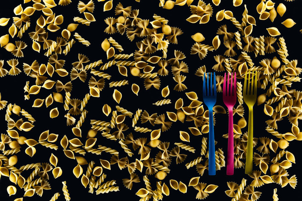 top view of plastic colorful forks on mixed uncooked pasta isolated on black  - Photo, Image