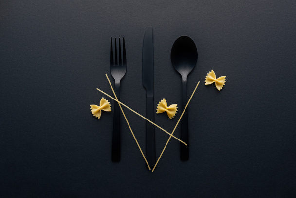 plastic cutlery with farfalle pasta and spaghetti on black background - Photo, Image