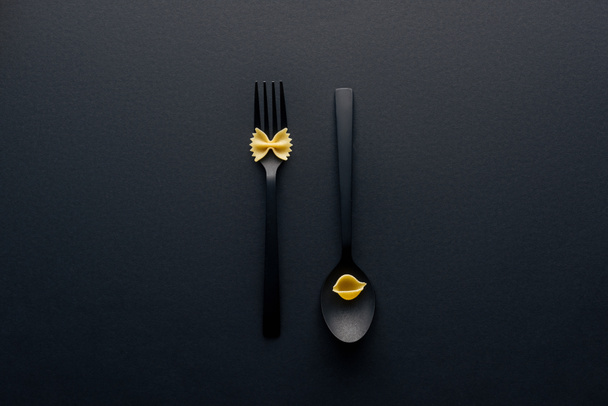 top view of spoon upside down with shell macaroni and fork with farfalle pasta on black background - Photo, Image