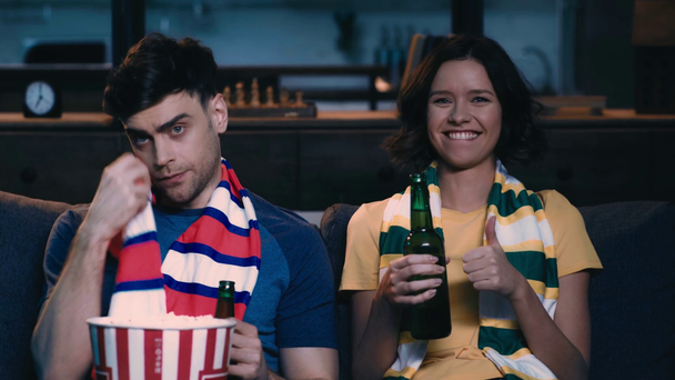 fiatal férfi nő a csíkos Sörös sört és étkezési Popcorn nézése közben labdarúgó mérkőzés a TV-otthon, lány mutatja győztes gesztus közelében ideges ember - Felvétel, videó