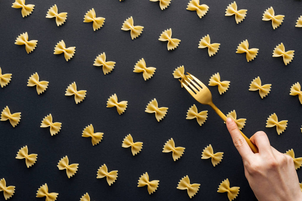 cropped view of woman trying to take farfalle pasta with plastic yellow fork isolated on black - Фото, зображення