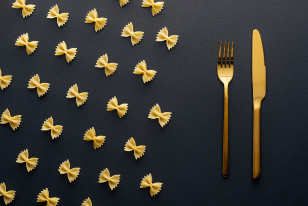 flat lay of farfalle pasta near golden knife and fork on black background - Photo, image